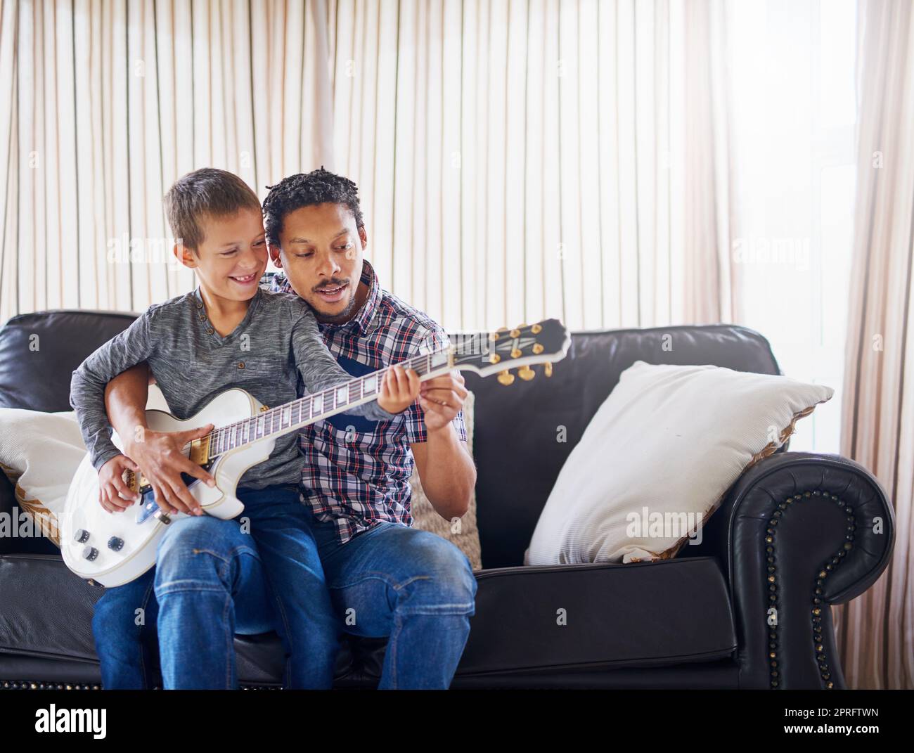 Seinem Sohn eine neue Melodie beibringen. Ein Vater lehrt seinem Sohn, wie er zu Hause Gitarre spielen kann. Stockfoto