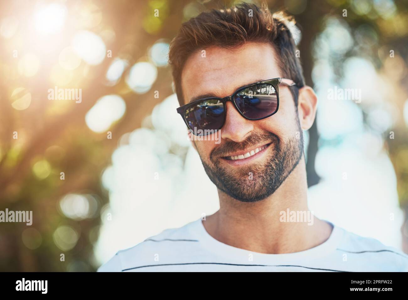 Hält seinen Look cool für die heißen Tage. Beschnittenes Porträt eines hübschen jungen Mannes, der an einem Sommertag im Freien eine Sonnenbrille trägt. Stockfoto