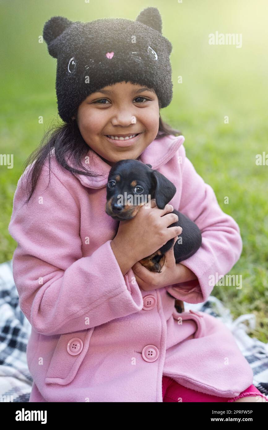 Einfach unvergleichlich... die Liebe der Welpen. Das verkürzte Porträt eines niedlichen kleinen Mädchens, das ihren Welpen kuschelt, während es draußen sitzt. Stockfoto