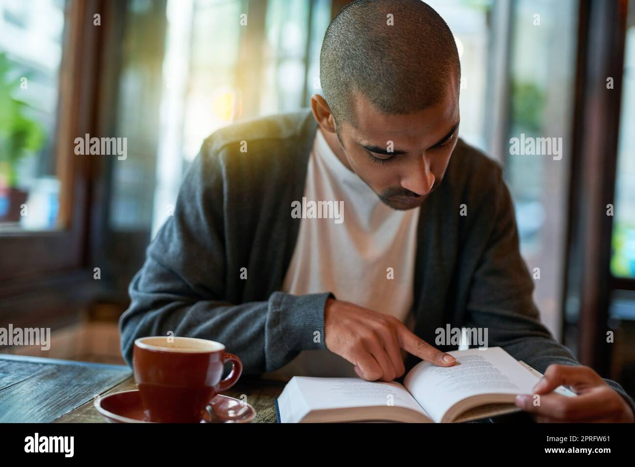 Eingetaucht in eine gute Lektüre. Ein junger Mann, der in einem Café ein Buch liest. Stockfoto