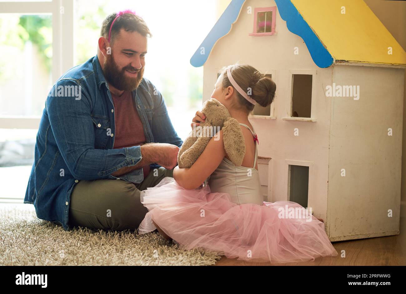 Ein entzückendes kleines Mädchen und ihr Vater spielen mit einem Puppenhaus zusammen zu Hause. Stockfoto