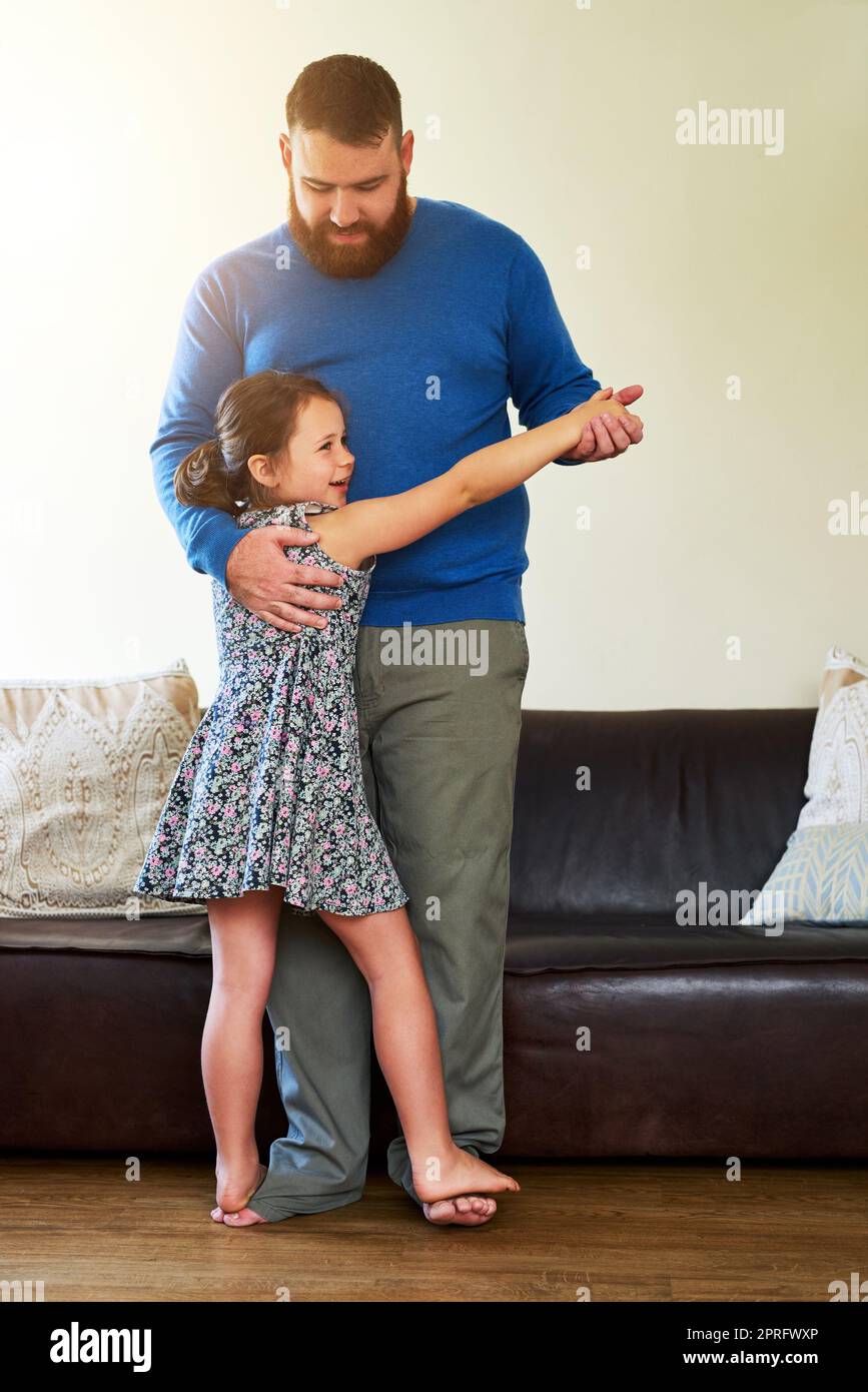 Die Vaterschaft Schritt für Schritt. Ein entzückendes kleines Mädchen, das zu Hause mit ihrem Vater tanzt. Stockfoto