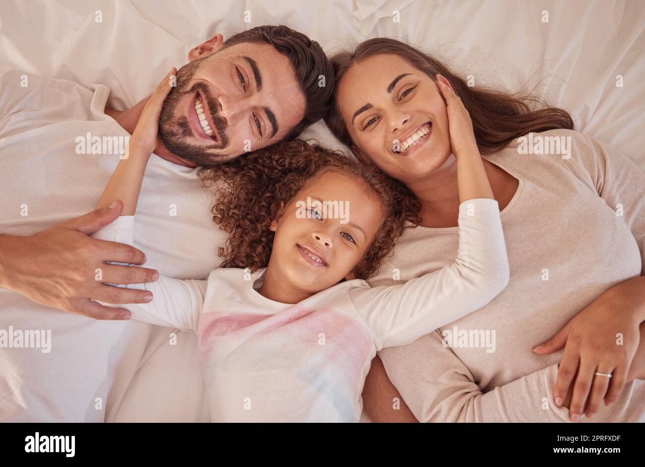 Porträt von glücklichen Eltern und Tochter mit Lächeln im Bett, während Sie sich am Morgen entspannen. Familie oder mutter, Vater und Kind, die im Schlafzimmer liegen, verspielten Spaß haben und sich zu Hause mit dem Glück verbinden Stockfoto