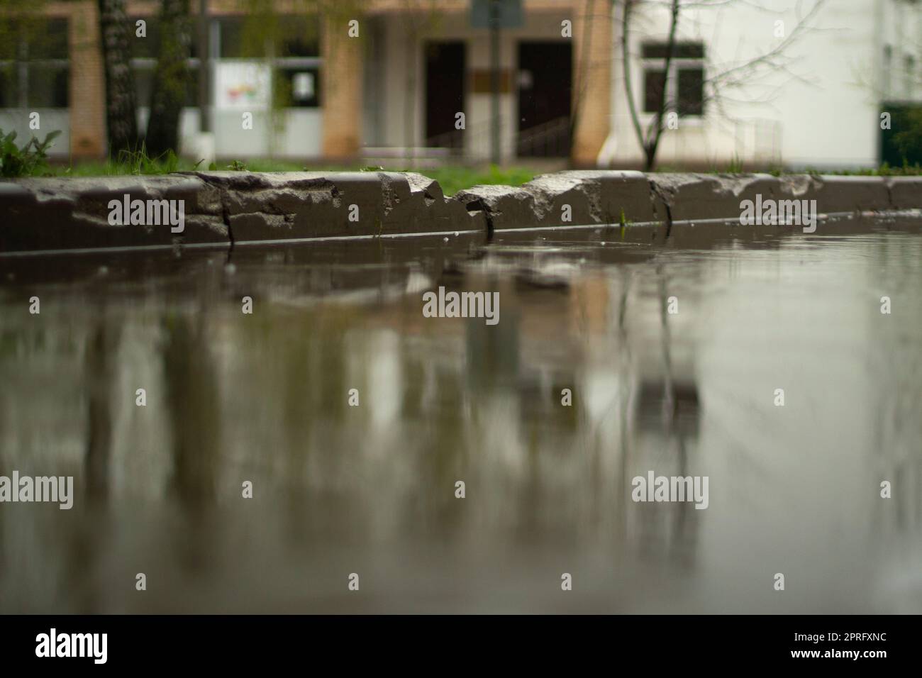 Regen draußen. Große Pfütze im Hof. Nasses Wetter. Oberfläche der Pfütze. Wasser auf der Straße. Stockfoto