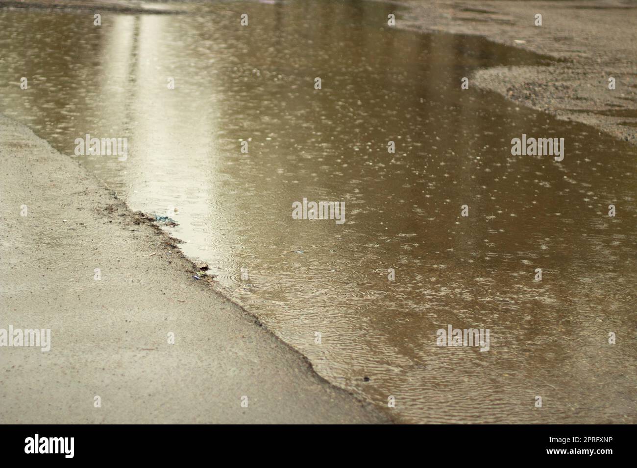 Regen draußen. Große Pfütze im Hof. Nasses Wetter. Oberfläche der Pfütze. Stockfoto