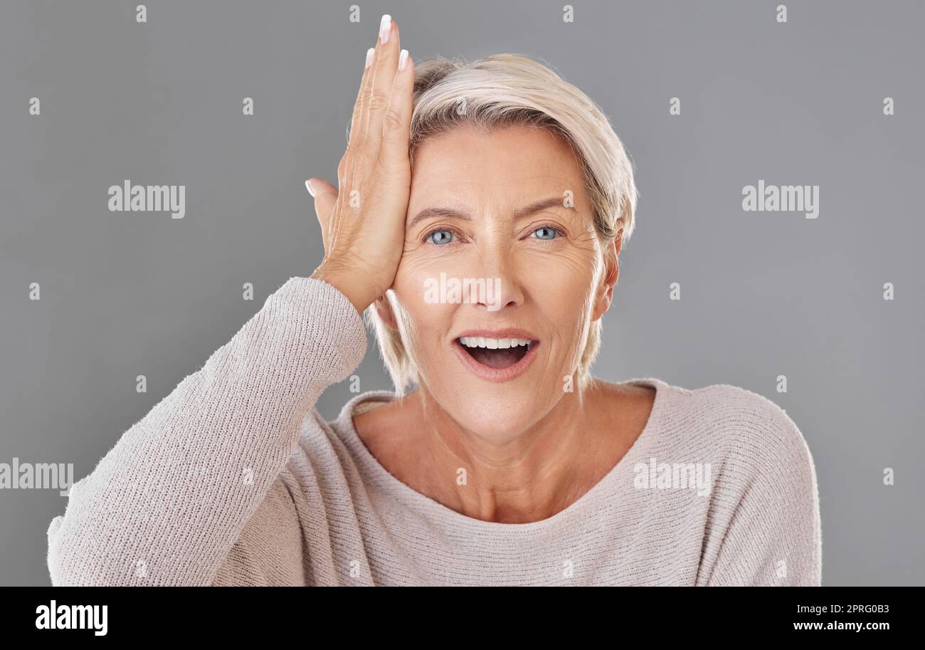 Denken, Ideen oder Erinnerungen mit einer Seniorin, die sich mit der Hand den Kopf klopft, um sich im Studio zu erinnern oder zu vergessen, auf grauem Hintergrund. Gesichtsporträt eines Modells mit grauen Haaren und einem Glühbirnenmoment Stockfoto