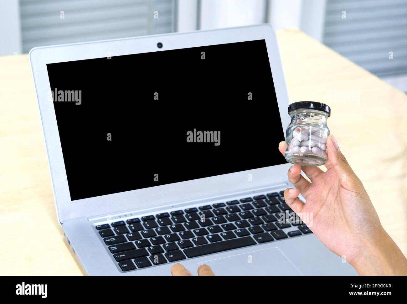 Nahaufnahme Hand hält Glas Pille Packer Flasche mit Kappe vor dem schwarzen Bildschirm Laptop-Computer. Stockfoto