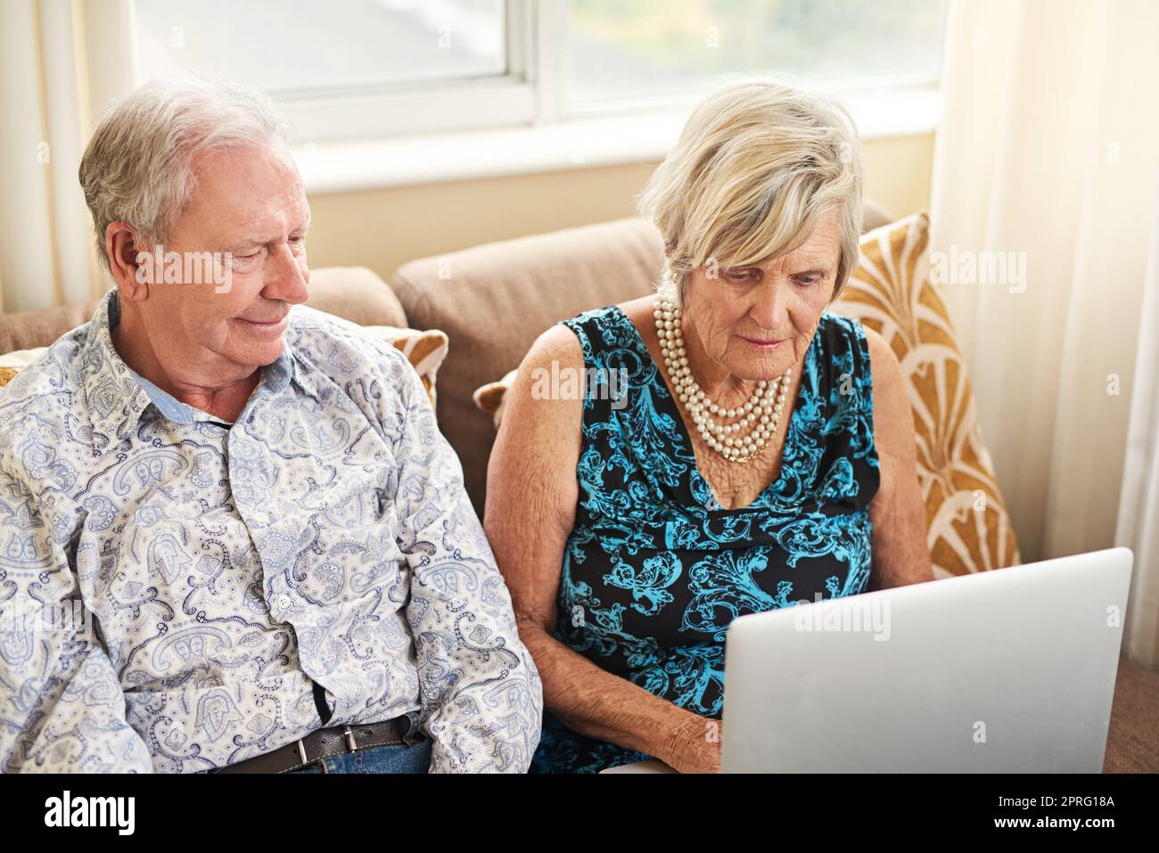 In der Nähe von Zuhause und der Außenwelt. Ein Seniorenpaar, das zu Hause einen Laptop auf dem Sofa zusammen benutzt. Stockfoto