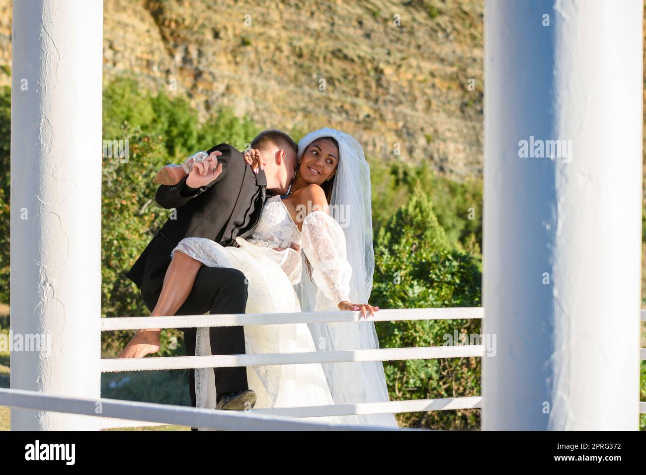 Junge schöne interracial Brautpaar Umarmung in der Pavillon, küsst der Kerl den Hals des Mädchens Stockfoto