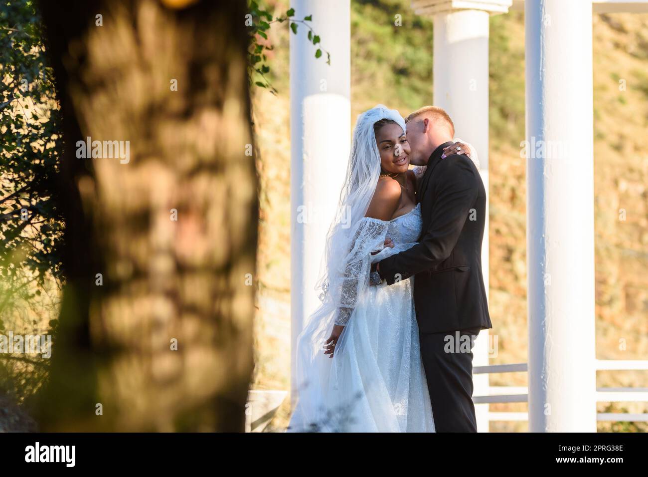 Junge schöne interracial Jungvermählte umarmt vor dem Hintergrund der weißen Säulen Stockfoto