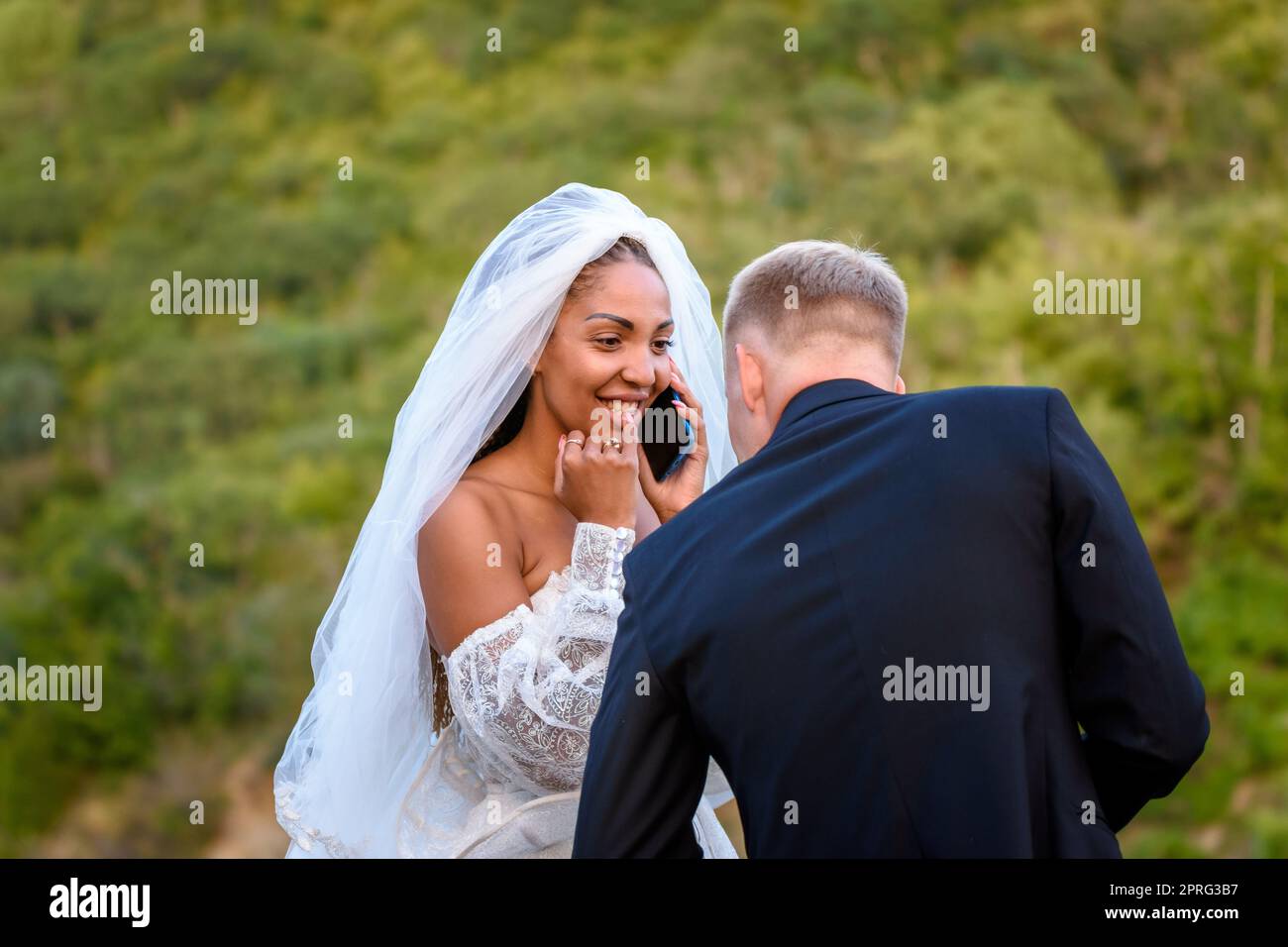 Eine schwarze Braut nimmt Glückwünsche am Telefon entgegen und schaut glücklich auf ihren weißen Ehemann Stockfoto