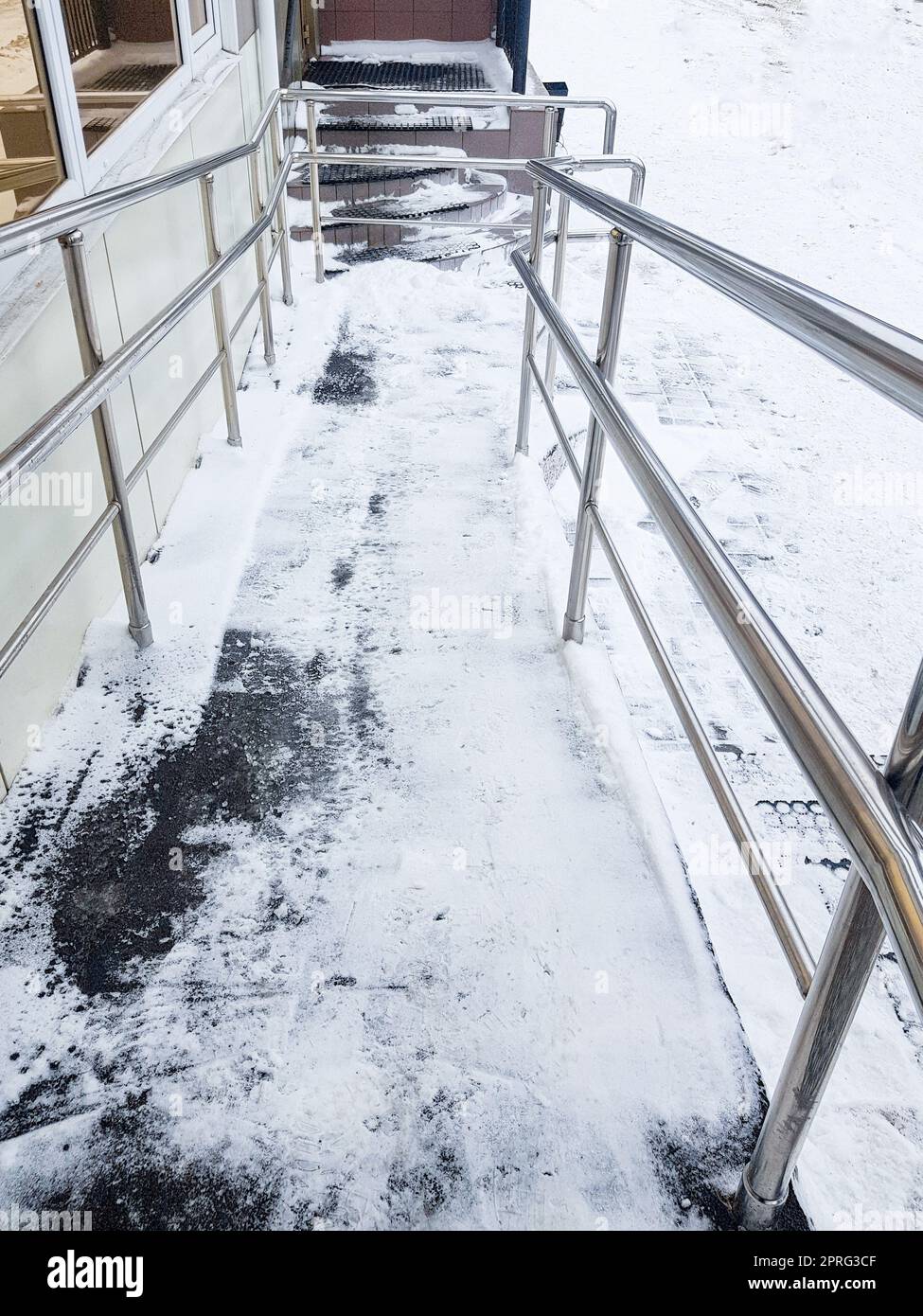 Moderne Rampe mit Metallgeländern für behinderte Menschen, schneebedeckte Rampe, Draufsicht, vertikales Foto Stockfoto