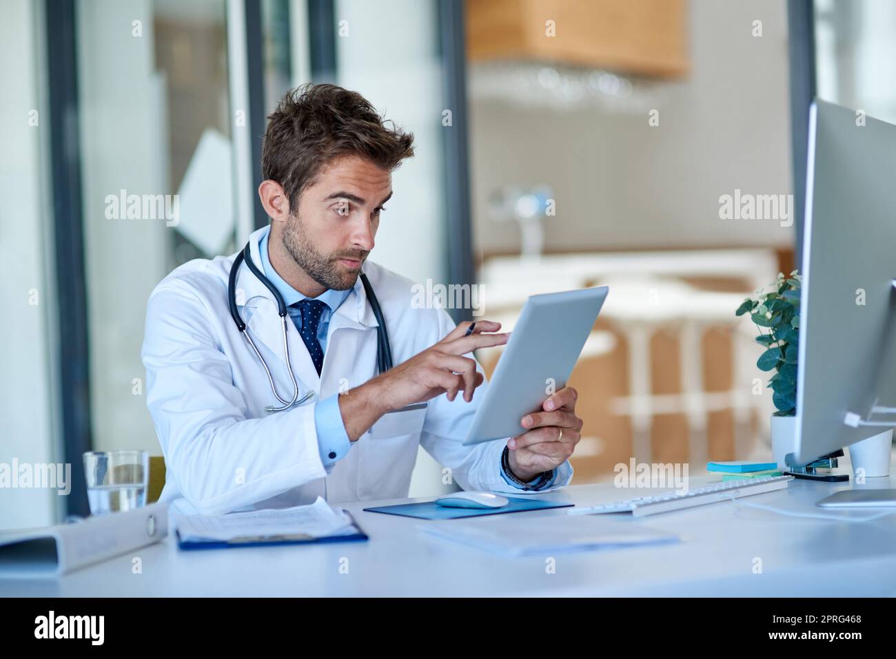 Technologie ist jeder Praktizierende bester Freund. Ein junger Arzt, der in seinem Büro an einem digitalen Tablet arbeitet. Stockfoto