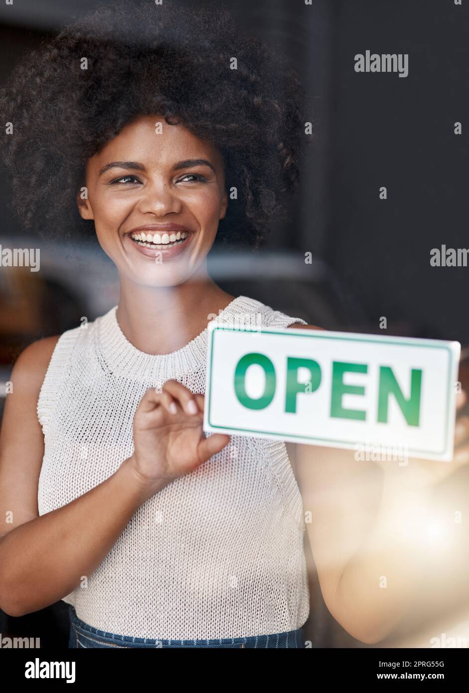 Eine lächelnde junge Geschäftsbesitzerin, die ein offenes Schild am Fenster ihres Cafés hält. Stockfoto