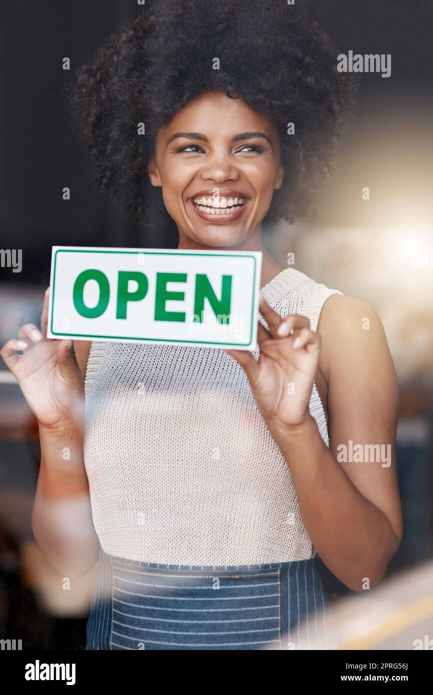 Es ist der Moment, für den sie gearbeitet haben. Eine lächelnde junge Geschäftsbesitzerin, die ein offenes Schild am Fenster ihres Cafés hält. Stockfoto
