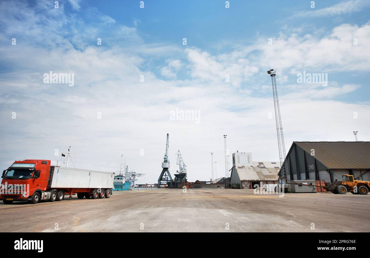 Logistik, Lieferkette oder Versand mit einer Fabrik, einem Lager oder einer Anlage im Hintergrund eines Hafens und einem Lkw und Kran am Dock. Lieferung, Fracht und Transport in der Export- und Importindustrie Stockfoto