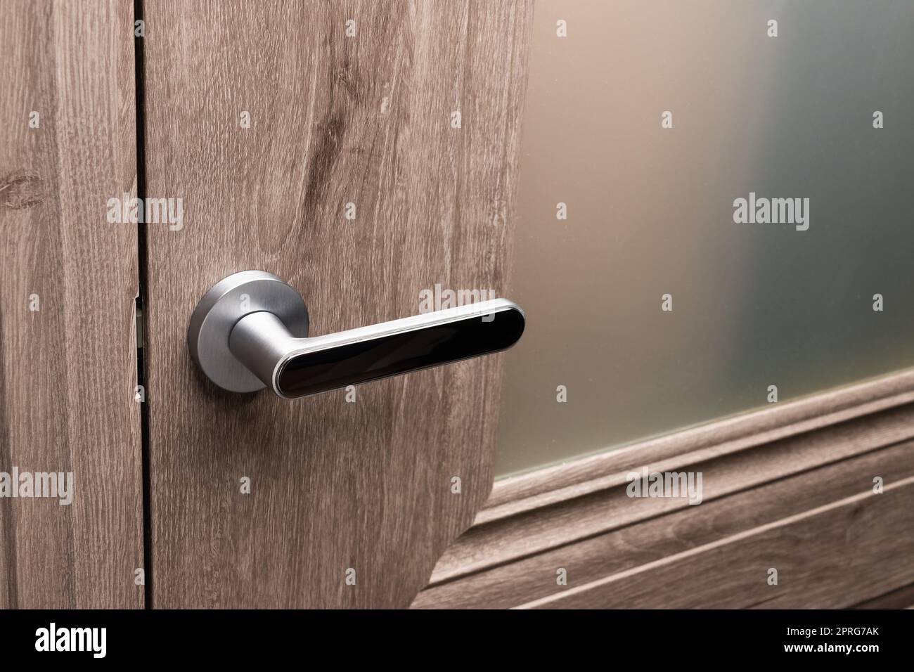Nahaufnahme des Türgriffs aus Stahl an der braunen Holztür. Stockfoto