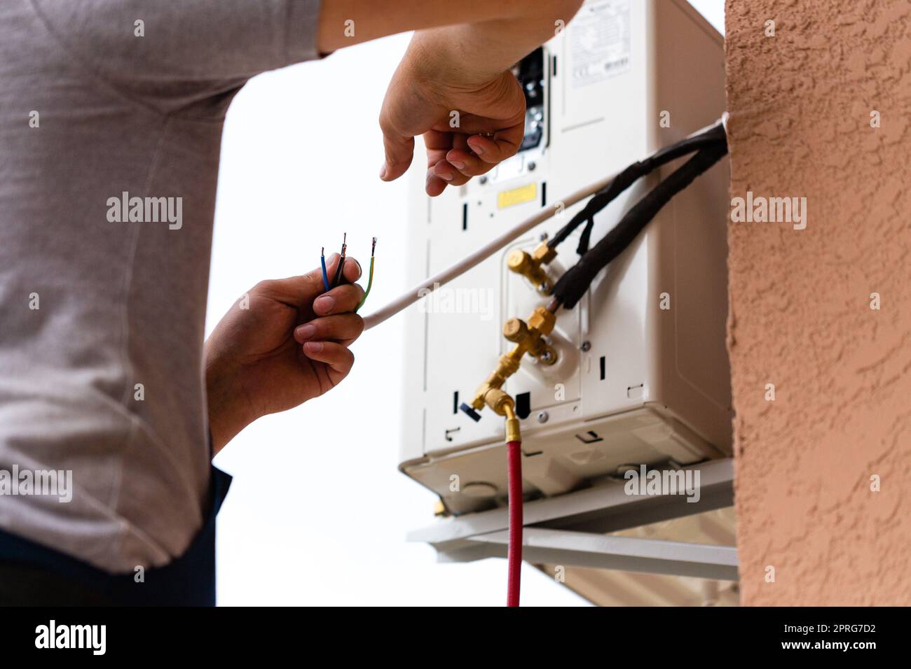 Männlicher Arbeiter verbindet elektrische Leitungen während der Installation der Klimaanlage. Stockfoto