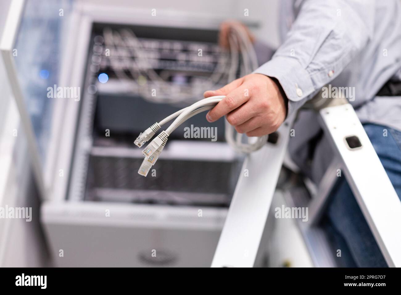 Männlicher Mitarbeiter konfiguriert das lokale Netzwerk, indem er Kabel und Stecker hält, um eine Verbindung zum Server herzustellen. Stockfoto