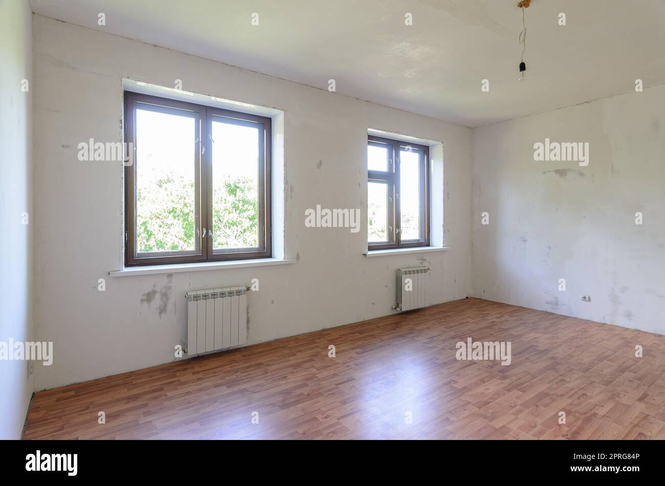 Das Innere eines leeren Raumes während der Renovierung gibt es zwei große Fenster im Raum, Heizkörper unter ihnen Stockfoto