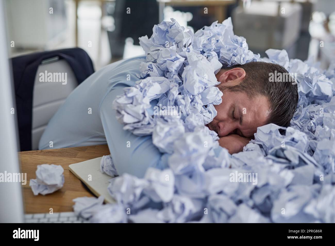 Der Stapel wird immer größer. Ein junger Geschäftsmann, umgeben von Papierstapeln in einem Büro. Stockfoto