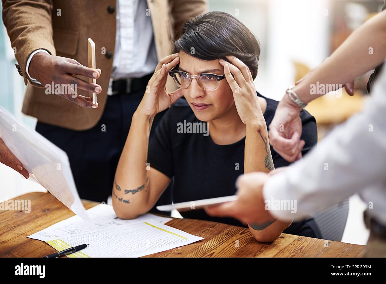 Ich kann mich nicht mit den Anforderungen aller auseinandersetzen. Eine gestresste Geschäftsfrau, umgeben von Kollegen, die Hilfe in einem Büro benötigen. Stockfoto