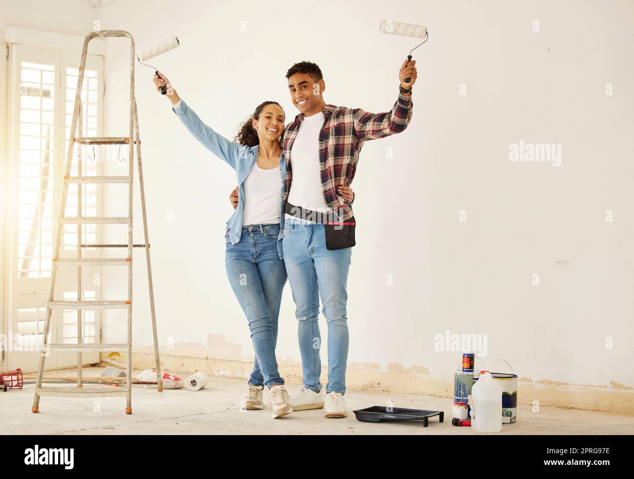 Porträt eines glücklichen Paares, das das neue Wohnzimmer in einem Haus oder einer Wohnung streicht. Mann und Frau mit Pinsel zur Dekoration einer Wandfarbe und Renovierung der Inneneinrichtung mit Lächeln oder Glück zusammen Stockfoto