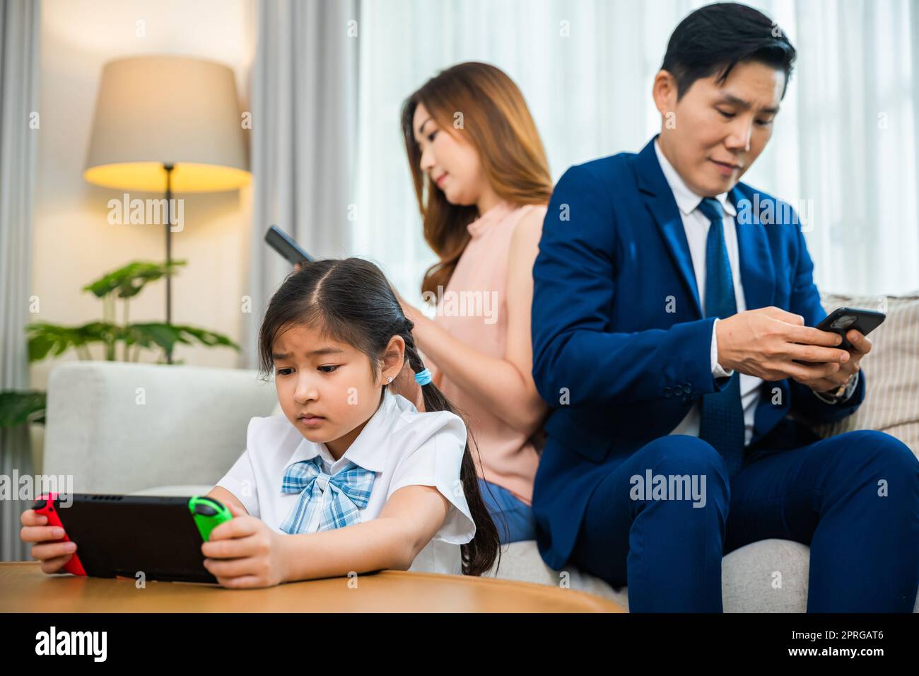 Asiatische Eltern ignorieren ihr Kind und schauen zu Hause auf ihr Handy Stockfoto