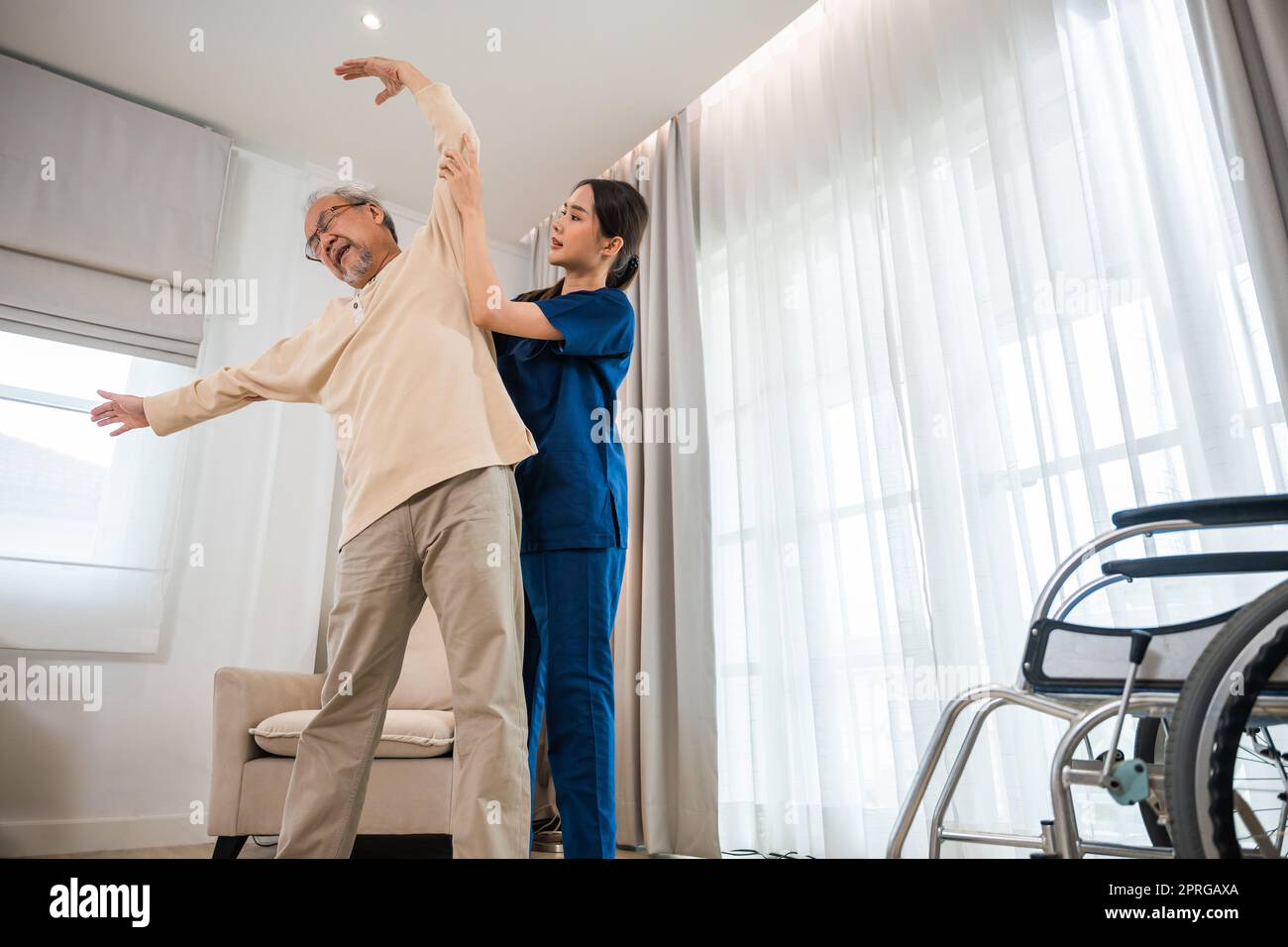 Der alte Senior-Mann trainiert zu Hause gern mit einem Physiotherapeuten für ausgestreckte Arme Stockfoto