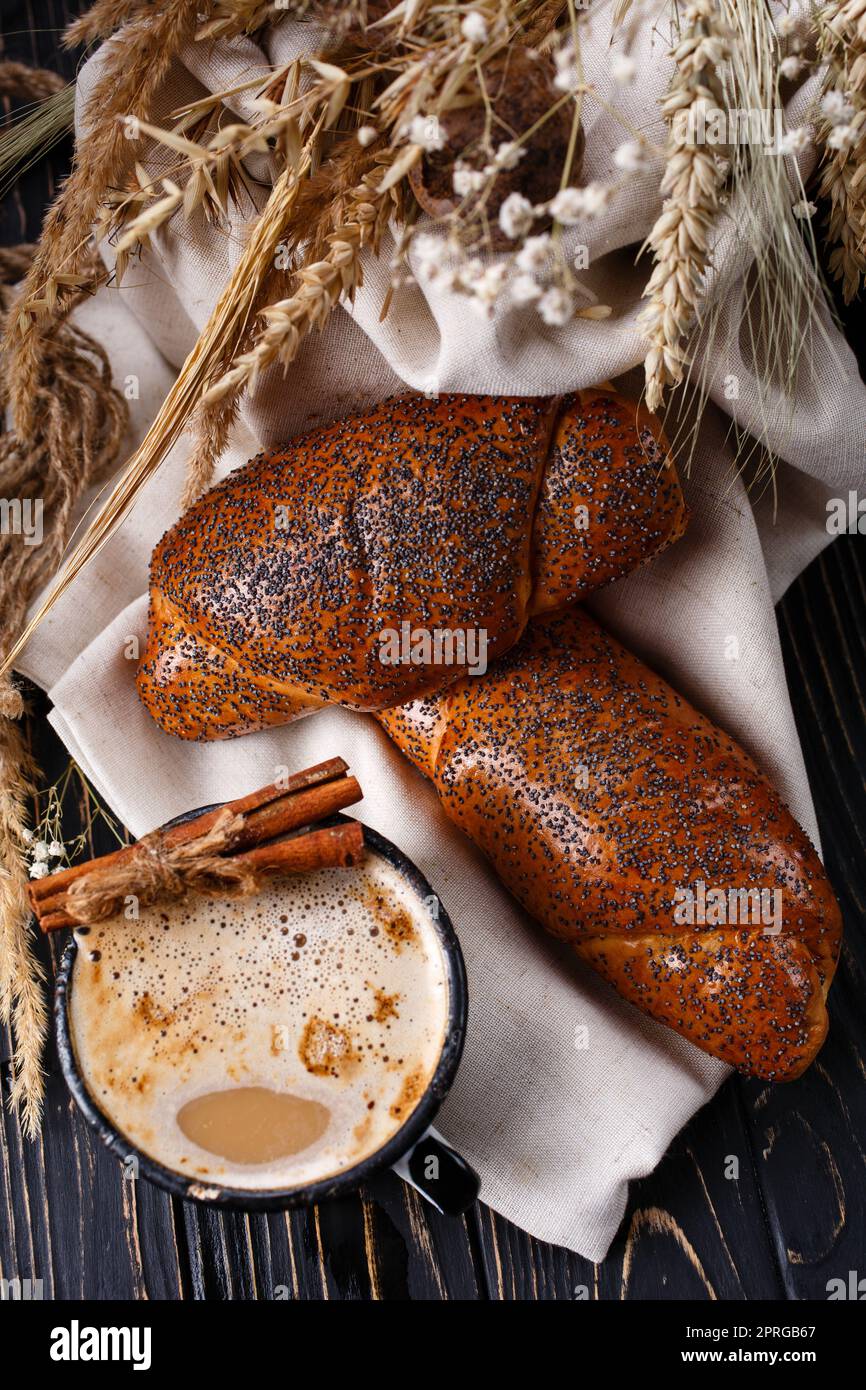 Frisch gebackene Brötchen mit Mohn und Kaffee auf rustikalem dunklen Holztisch. Stockfoto