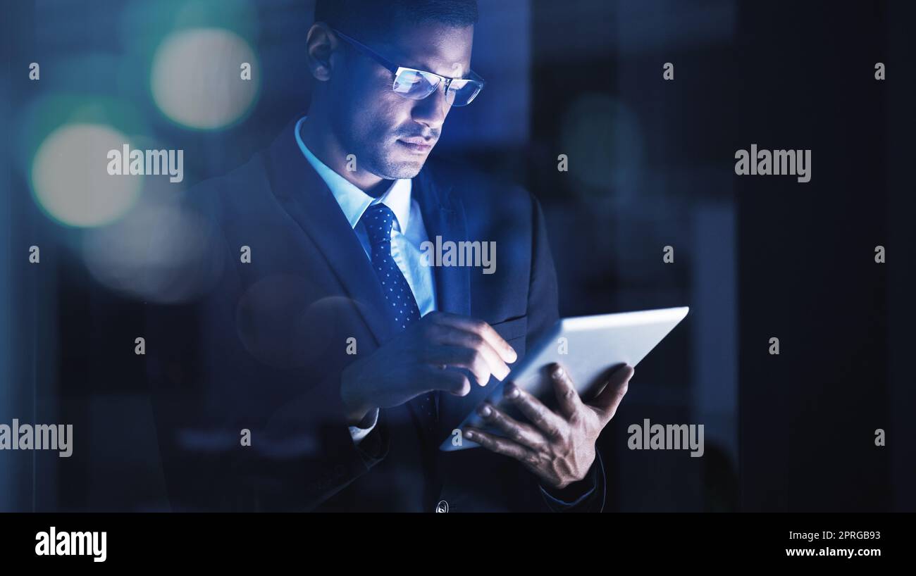 Ein Geschäftsmann, der Überstunden in einem modernen Firmenbüro mit einem digitalen Tablet und einer Brille macht. Unternehmensmanager liest Unternehmensdokumente, -Daten und -Statistiken auf einer Internet-Website mit Technologie. Stockfoto