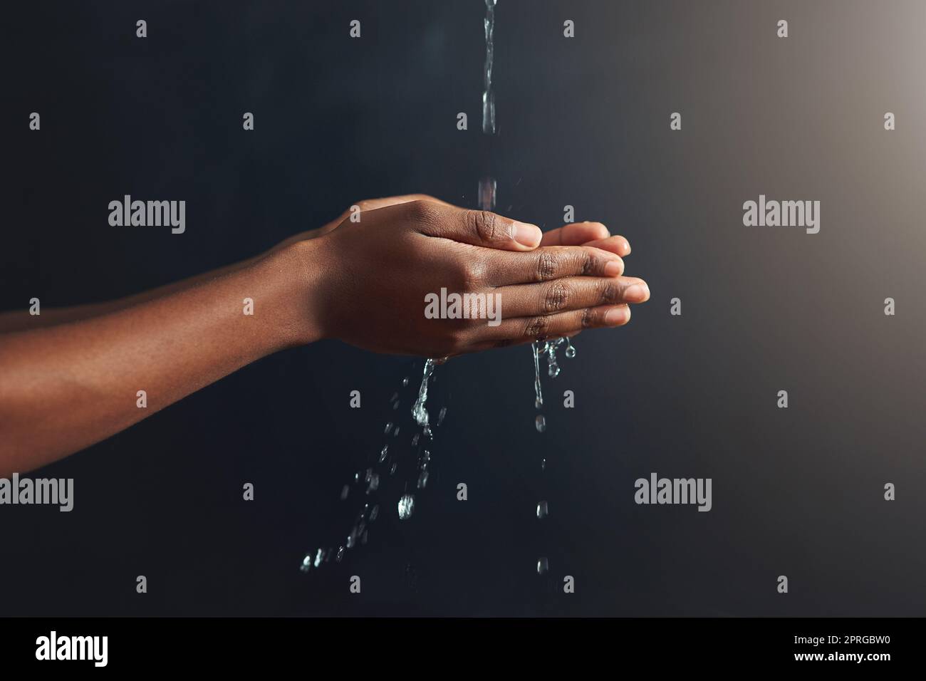Reinheit in der Handfläche. Hände, die unter einem Wasserstrahl vor einem grauen Hintergrund gehalten werden. Stockfoto