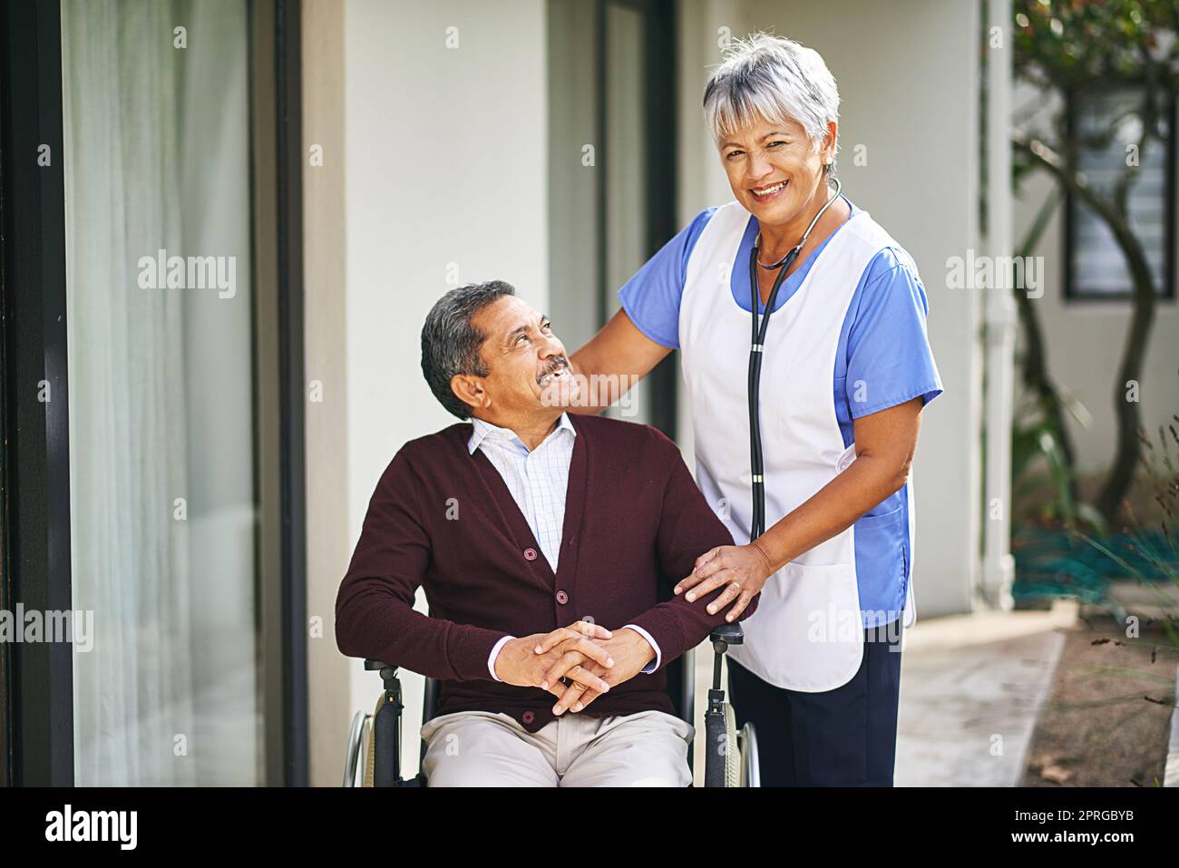 Freundlichkeit und Mitgefühl gehen einen langen Weg. Ein älterer Mann im Rollstuhl wird von einer Krankenschwester in einem Altersheim betreut. Stockfoto