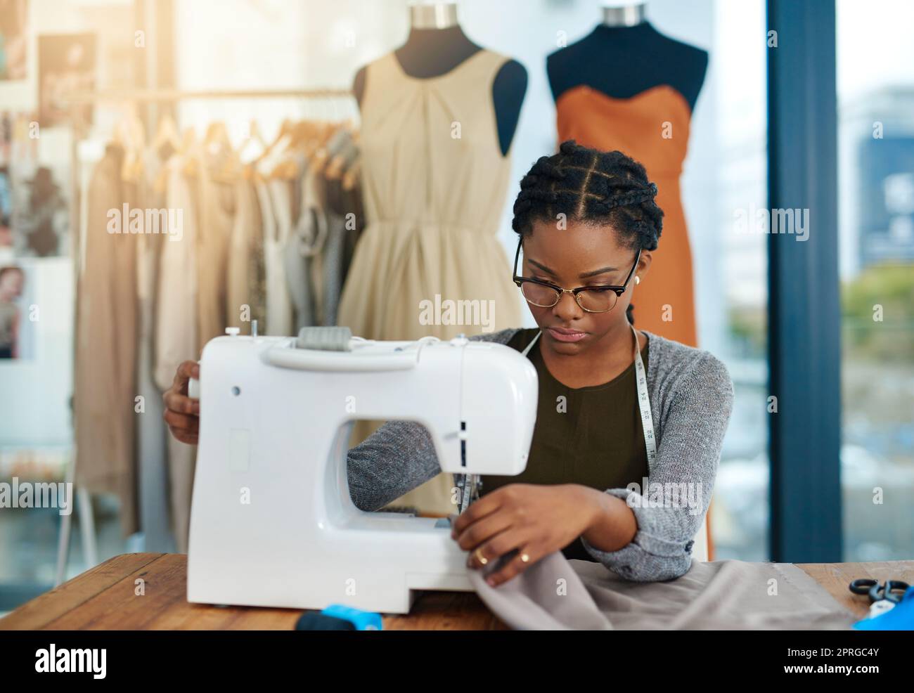 Eine junge Modedesignerin, die in ihrer Werkstatt eine Nähmaschine verwendet. Stockfoto