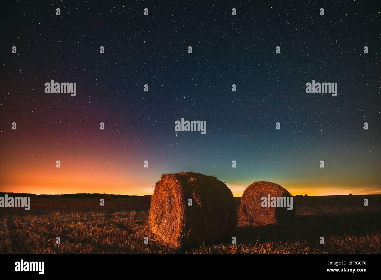 Comet Neowise C2020 F3 in Night Starry Sky über Heuhaufen im Summer Agricultural Field. Nachtstars Über Der Ländlichen Landschaft Mit Heuballen Nach Der Ernte. Landwirtschaftskonzept Stockfoto