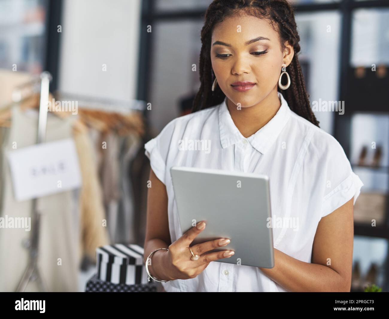 Online-Shopping hält unser Geschäft offen 247. Eine junge Geschäftsbesitzerin benutzt ihr Tablet, während sie in ihrem Geschäft steht. Stockfoto