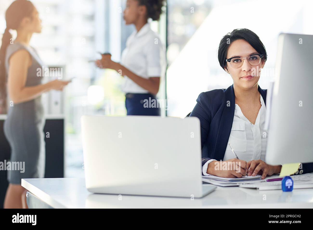 Auf ihre Karriereziele hinzuarbeiten. Zugeschnittenes Porträt einer Geschäftsfrau, die in ihrem Büro mit Kollegen im Hintergrund arbeitet. Stockfoto