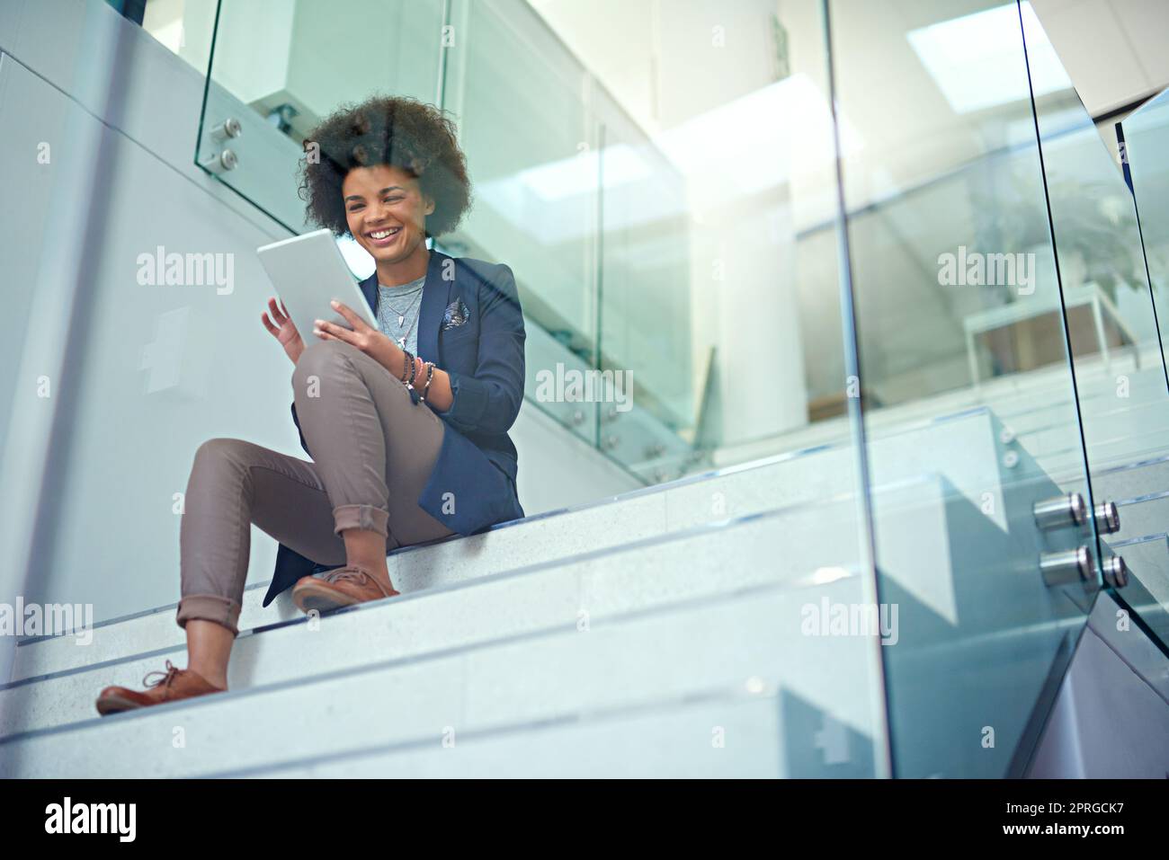 Online einige innovative Ideen durcharbeiten: Eine junge Geschäftsfrau, die in einem modernen Büro ein digitales Tablet auf der Treppe benutzt. Stockfoto