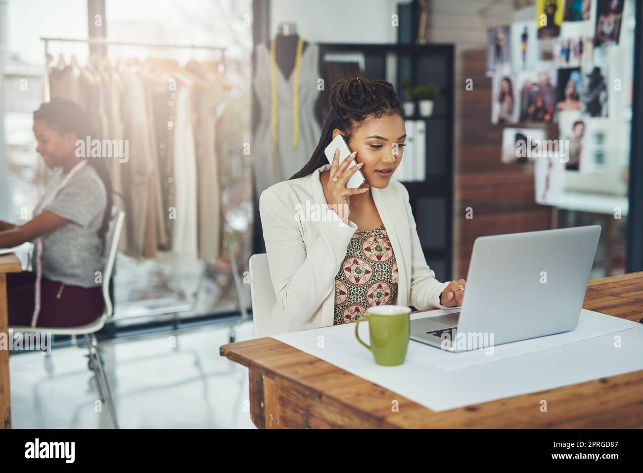 Eine Modedesignerin spricht auf ihrem Handy, während sie ihren Laptop benutzt. Stockfoto