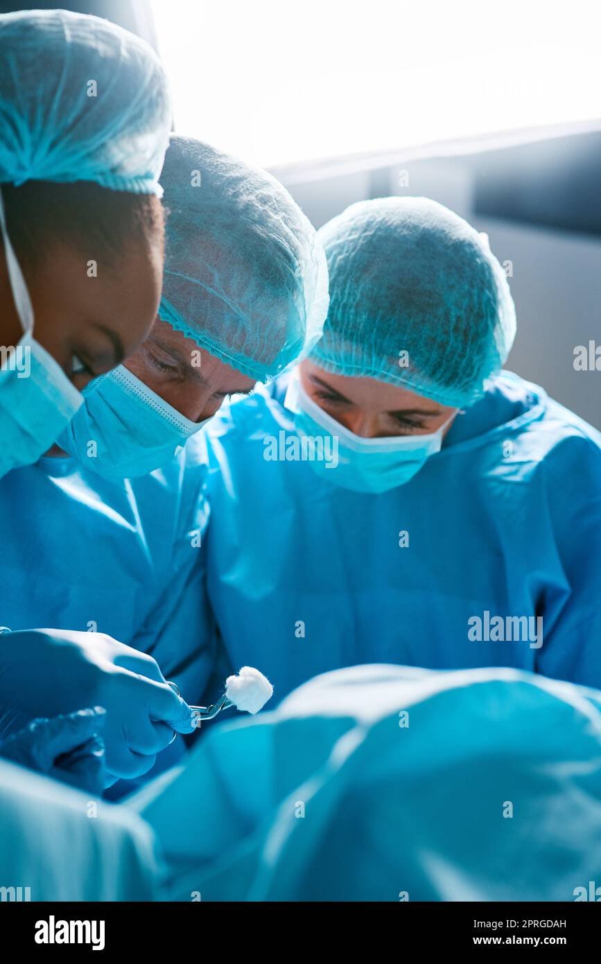 Feste Hände und ein starkes Engagement. Eine Gruppe von Chirurgen, die einen Patienten in einem Krankenhaus operiert. Stockfoto