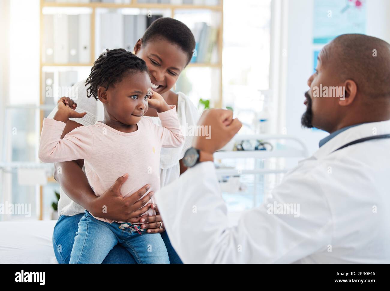 Kinderarzt mit schwarzer Familie, Baby und Mutter in Klinik oder Krankenhaus Check-up Termin für Wachstum Wellness. Kind in starkem Muskel Flex für Kalzium mit lustigen männlichen medizinischen Pädiatrie-Experten Stockfoto