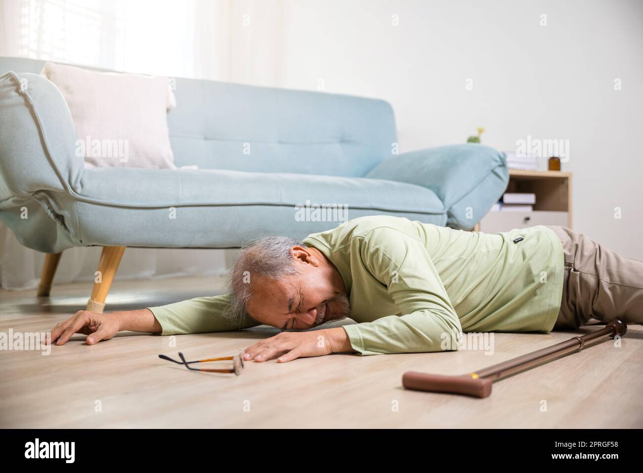 Kranker älterer Mann neben der Couch auf dem Teppich im Wohnzimmer zu Hause, älterer reifer Großvater, der einen Unfall hatte, nachdem er allein mit dem Gehen eine Physiotherapie gemacht hatte Stockfoto