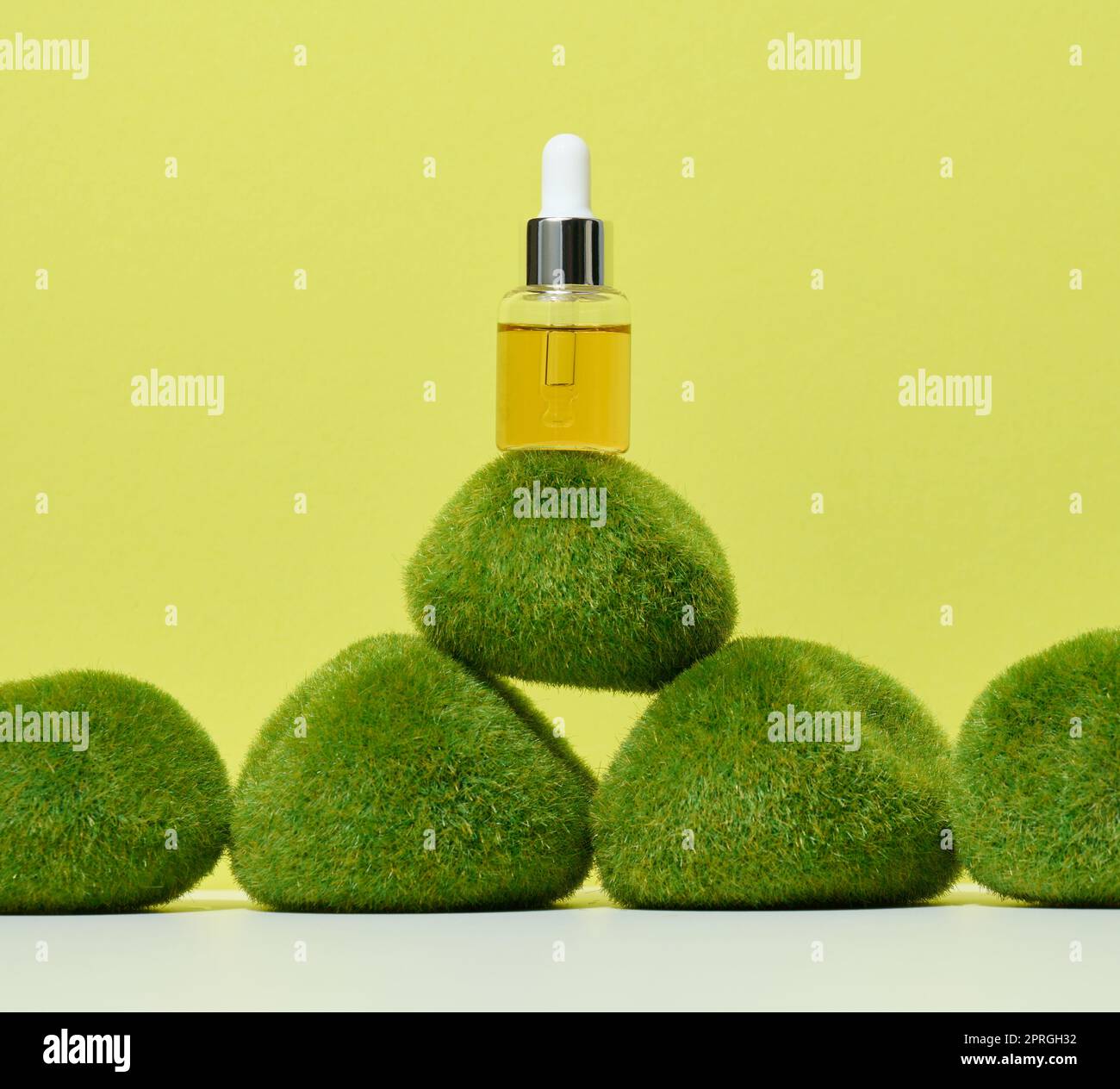 Transparente Glasflasche mit Pipette und gelbem Öl auf grünem Moos. Stockfoto
