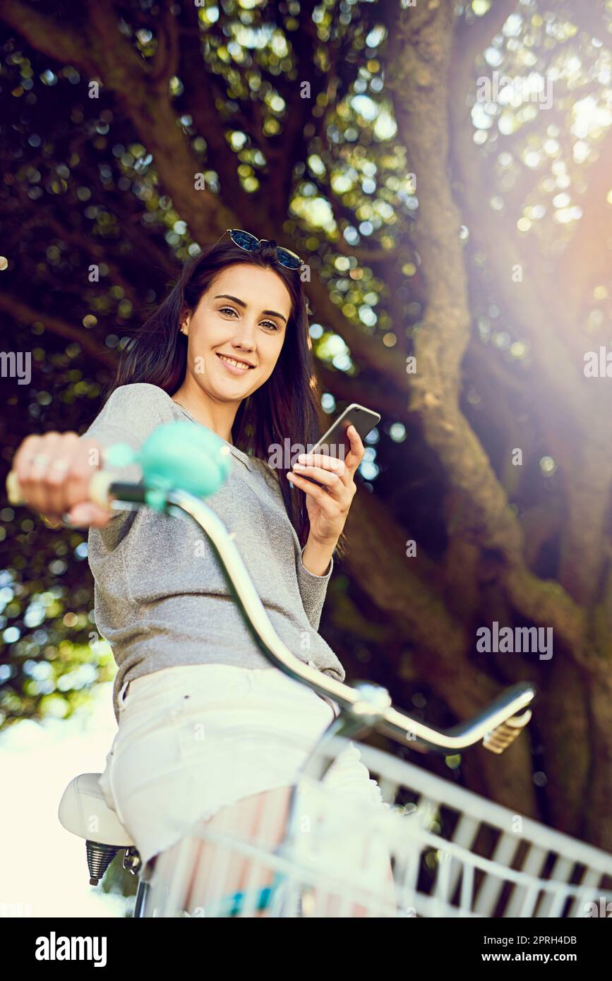Nur für eine gemütliche Fahrt. Porträt einer attraktiven jungen Frau, die ihr Handy benutzt, während sie auf dem Fahrrad fährt. Stockfoto