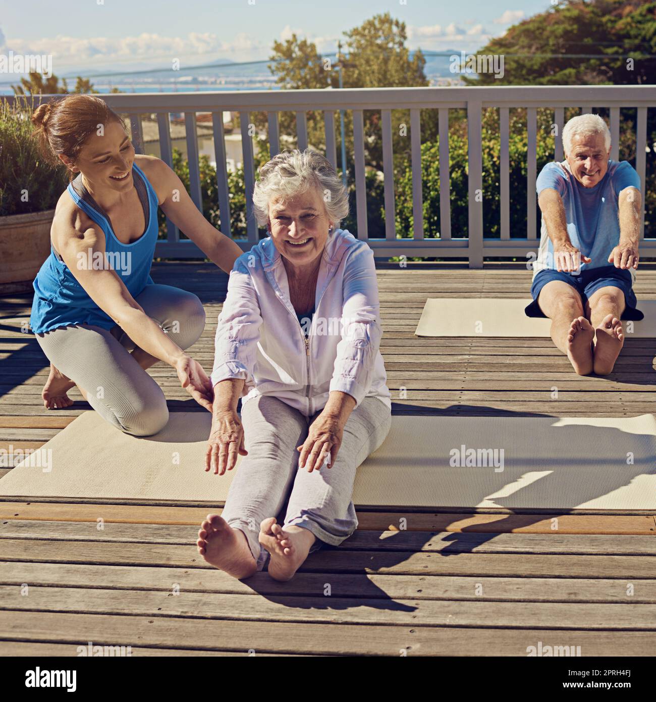 Fit und aktiv in ihren goldenen Jahren. Ein Seniorenpaar macht Yoga zusammen mit einem Lehrer auf ihrer Terrasse draußen. Stockfoto