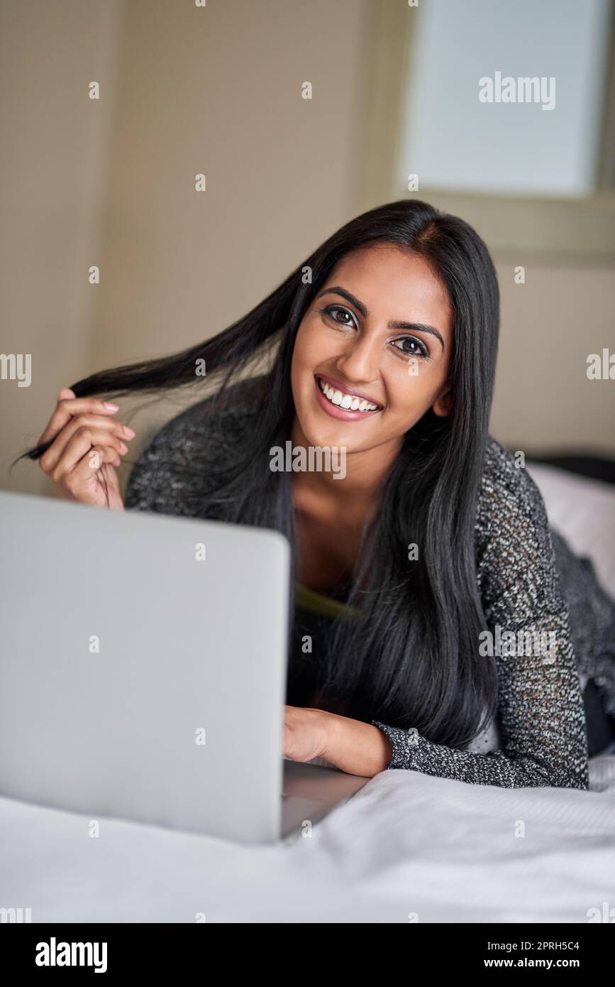 Tragbare Technologie bedeutet, das Leben in meinem Tempo zu leben. Porträt einer jungen Frau, die sich auf dem Bett entspannt und einen Laptop benutzt. Stockfoto