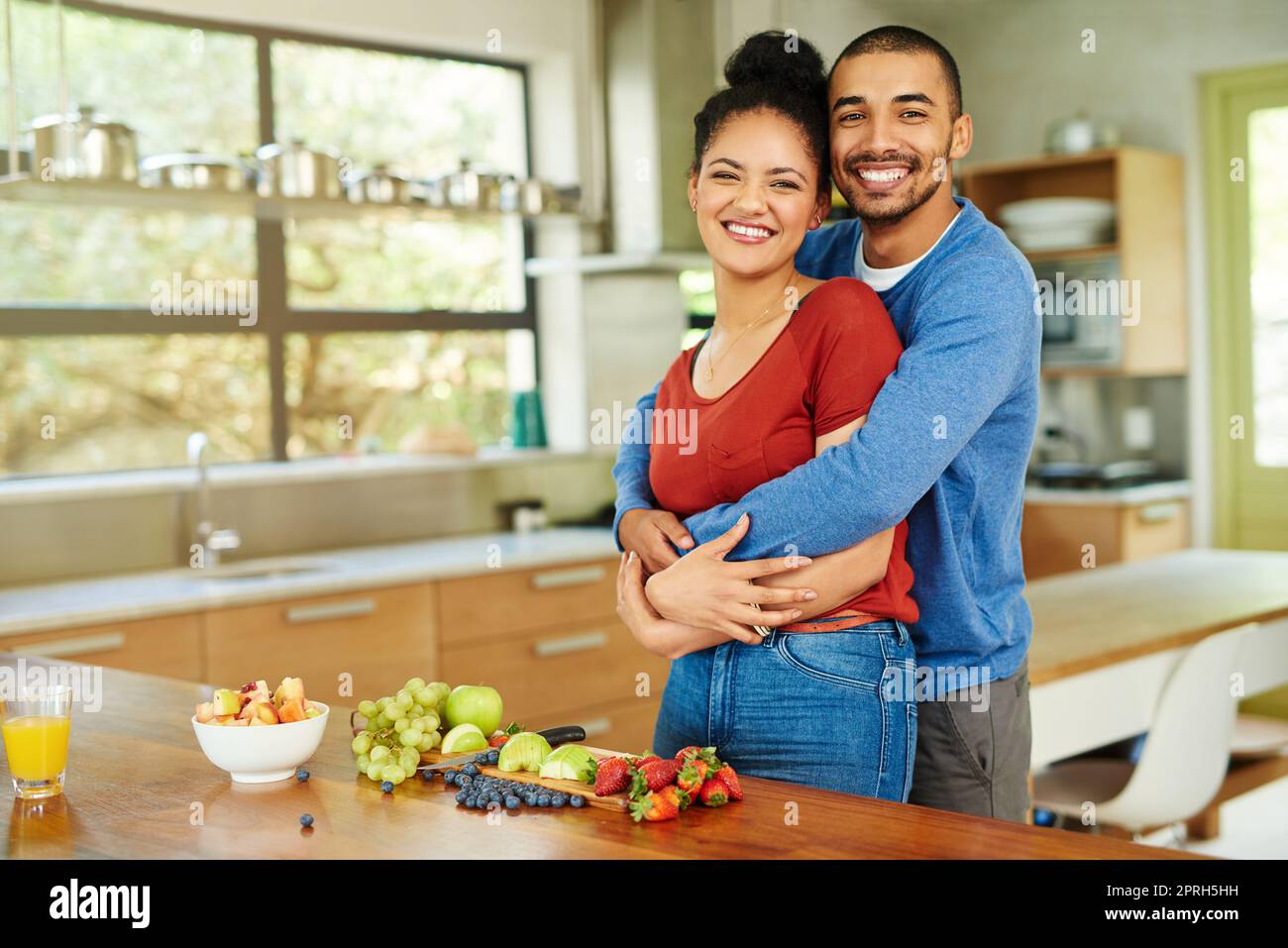 Haben unseren gesunden Lebensstil geliebt. Ein Porträt eines hübschen jungen Mannes, der seine Frau umarmt, während sie in der Küche einen Obstsalat macht. Stockfoto