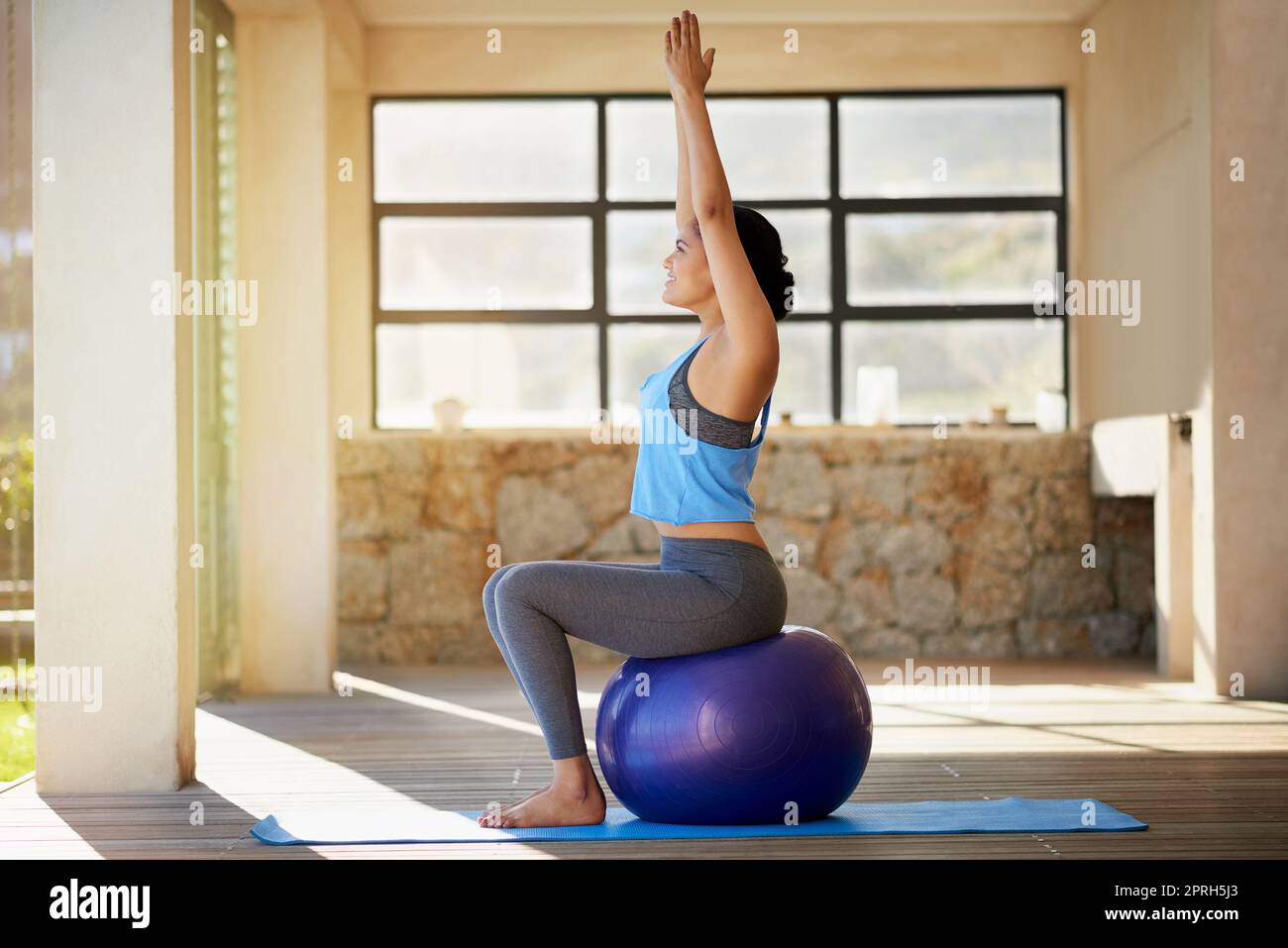 Mit Blick auf ihre Fitness-Ziele. Eine junge Frau, die zu Hause mit einem Gymnastikball trainiert. Stockfoto