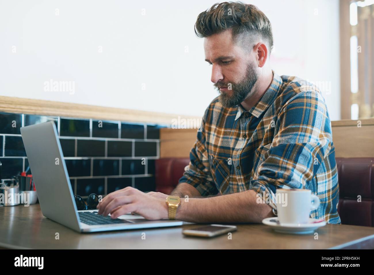 Manchmal braucht man nur einen Szenenwechsel. Ein junger Mann, der seinen Laptop benutzt, während er in einem Café sitzt. Stockfoto