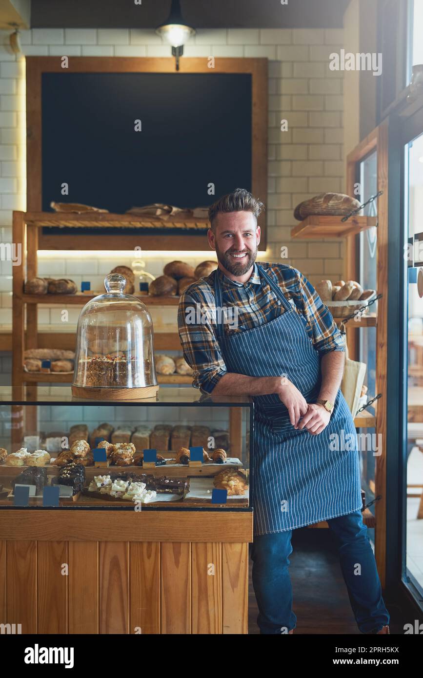 Probieren Sie etwas köstliches. Porträt eines jungen Geschäftsinhabers, der hinter der Theke in seiner Bäckerei steht. Stockfoto